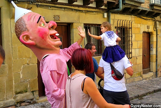A cabezudo high fives at toddler on her father's shoulders in Hondarribia, Spain