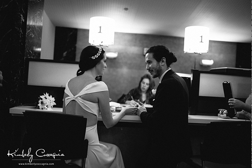 The bride and groom sit at a counter in NYC's city hall