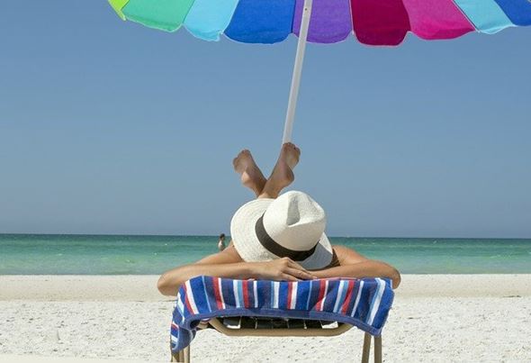 A woman wearing a hat lying face down on a chair on the beach